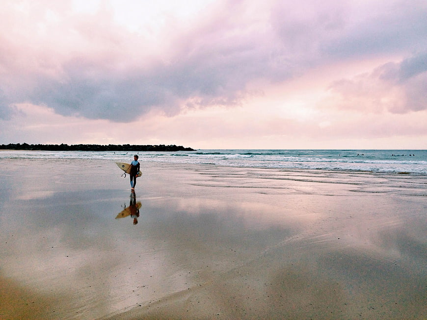 Surfer Walking on Wet Beach at Sunset