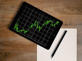 Tablet with green financial growth chart on wooden desk