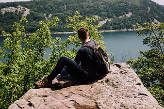 Hiker sitting on rock overlooking lake and forest
