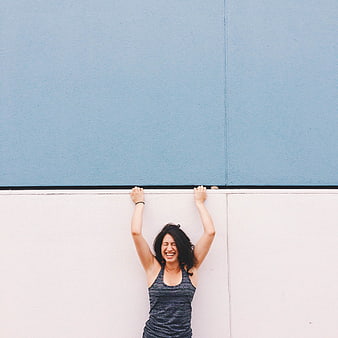 Laughing woman holding onto wall edge against blue and white background