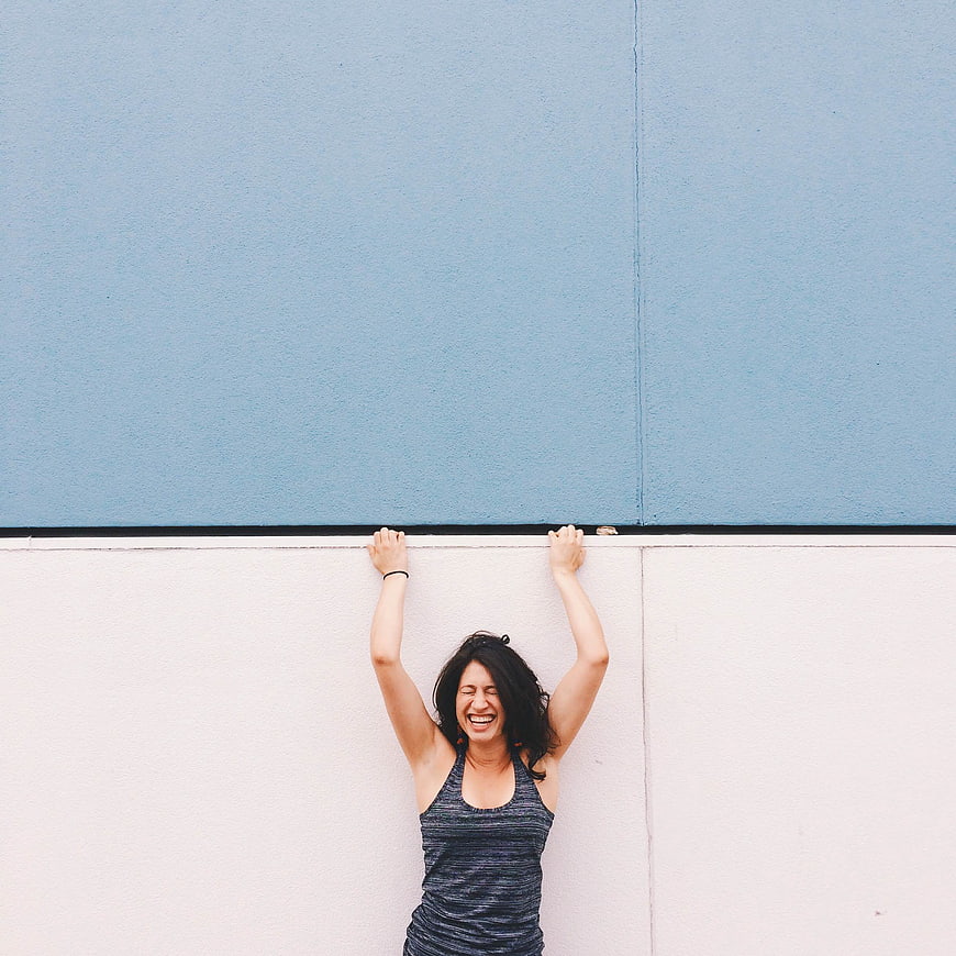 Laughing woman holding onto wall edge against blue and white background