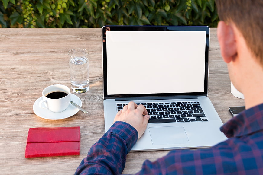 Man working on laptop with blank screen at outdoor cafe