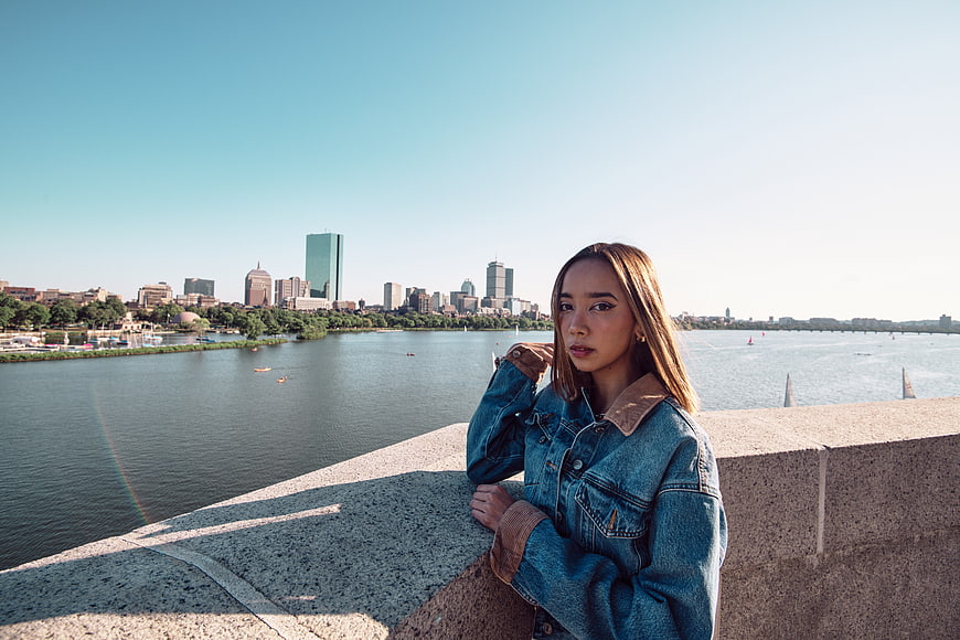 Young Asian Woman in Denim Jacket by River with City Skyline