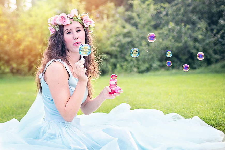 Young woman in blue dress blowing soap bubbles in park