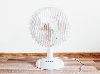 White electric fan on wooden floor against white wall