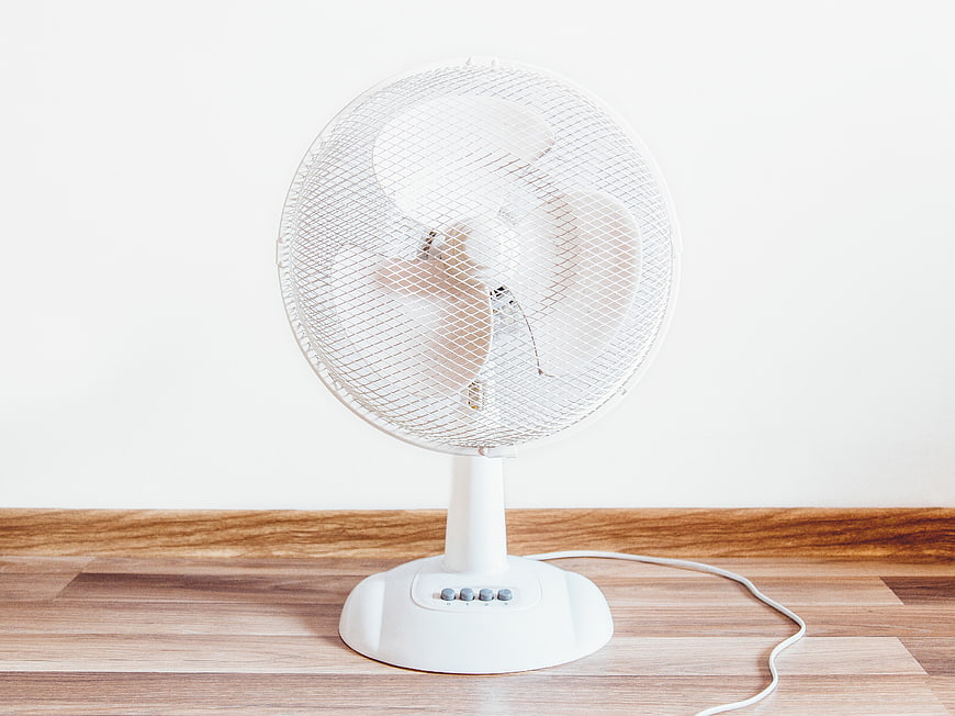 White electric fan on wooden floor against white wall