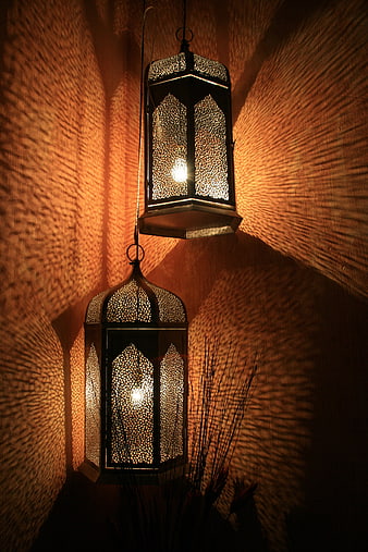 Two ornate hanging lanterns casting intricate warm light patterns on textured wall