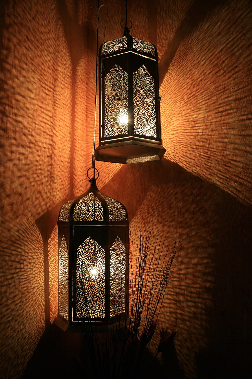 Two ornate hanging lanterns casting intricate warm light patterns on textured wall