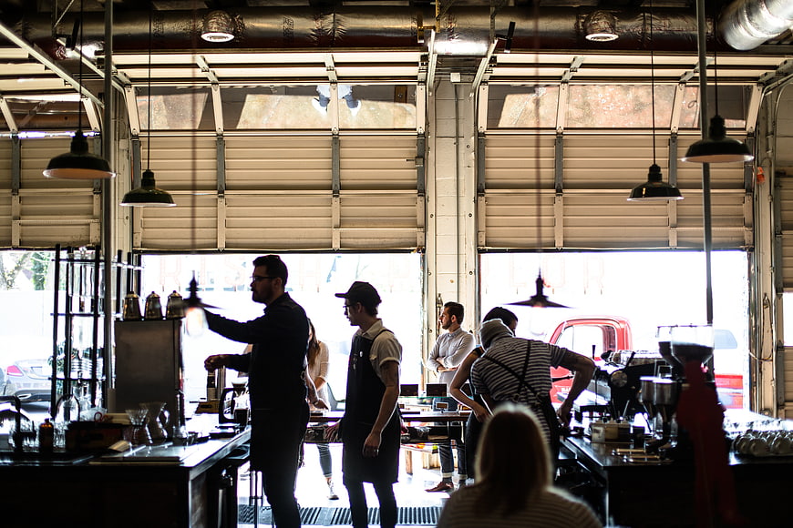 Baristas working in industrial coffee shop with garage doors