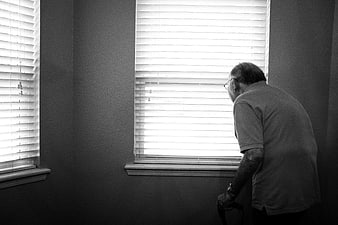 Senior man looking out window with blinds
