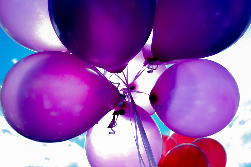 Low angle view of purple and red helium balloons against blue sky