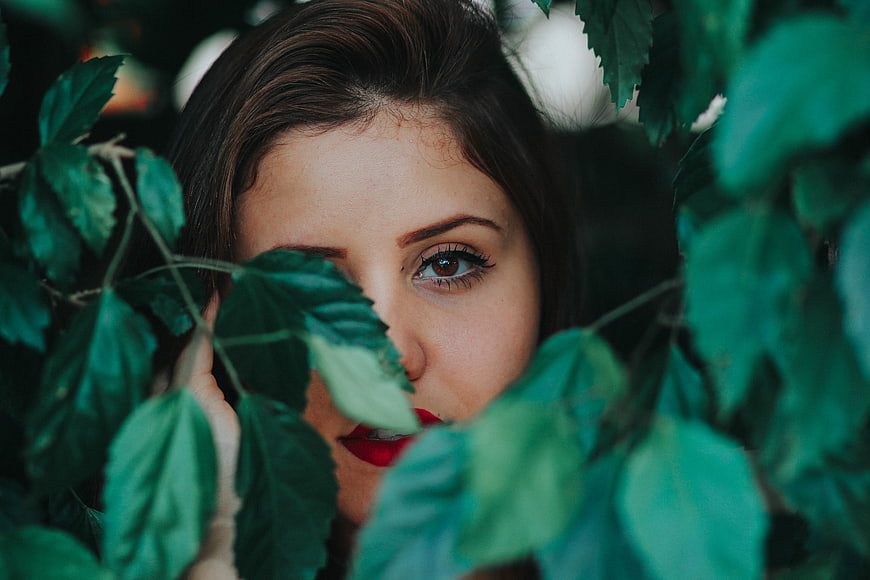 Woman with red lips peeking through green leaves