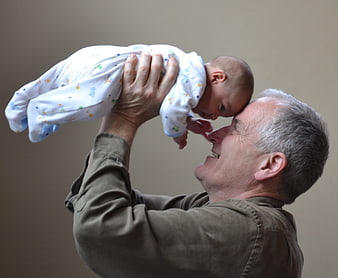 Senior grandfather lifting newborn baby in joy