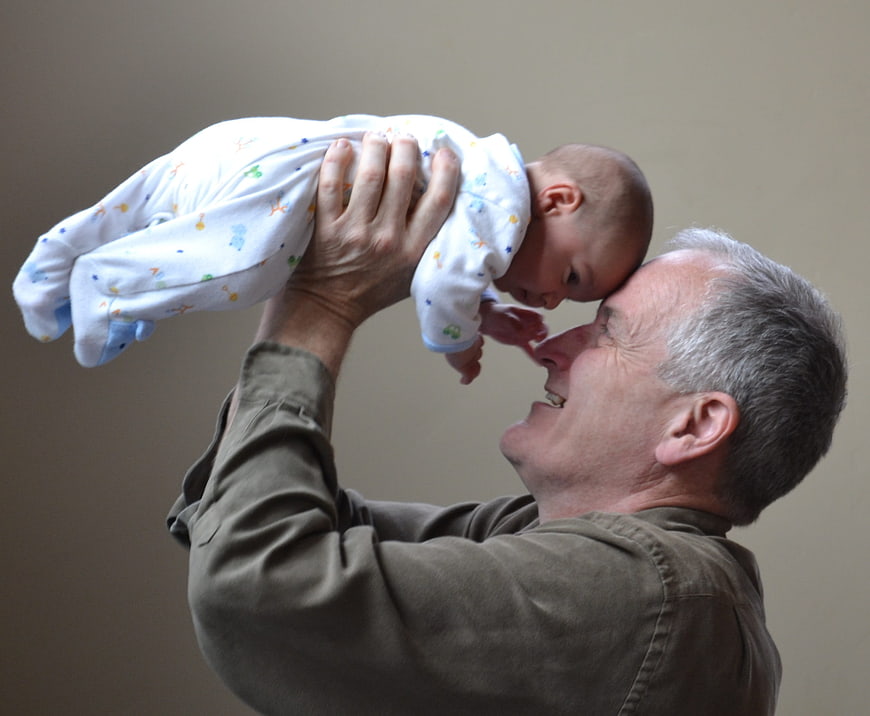 Senior grandfather lifting newborn baby in joy