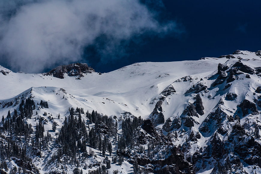 Snowy Mountain Peaks with Pine Forest and Clouds
