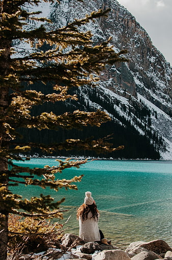 Woman sitting by turquoise alpine lake with snowy mountains