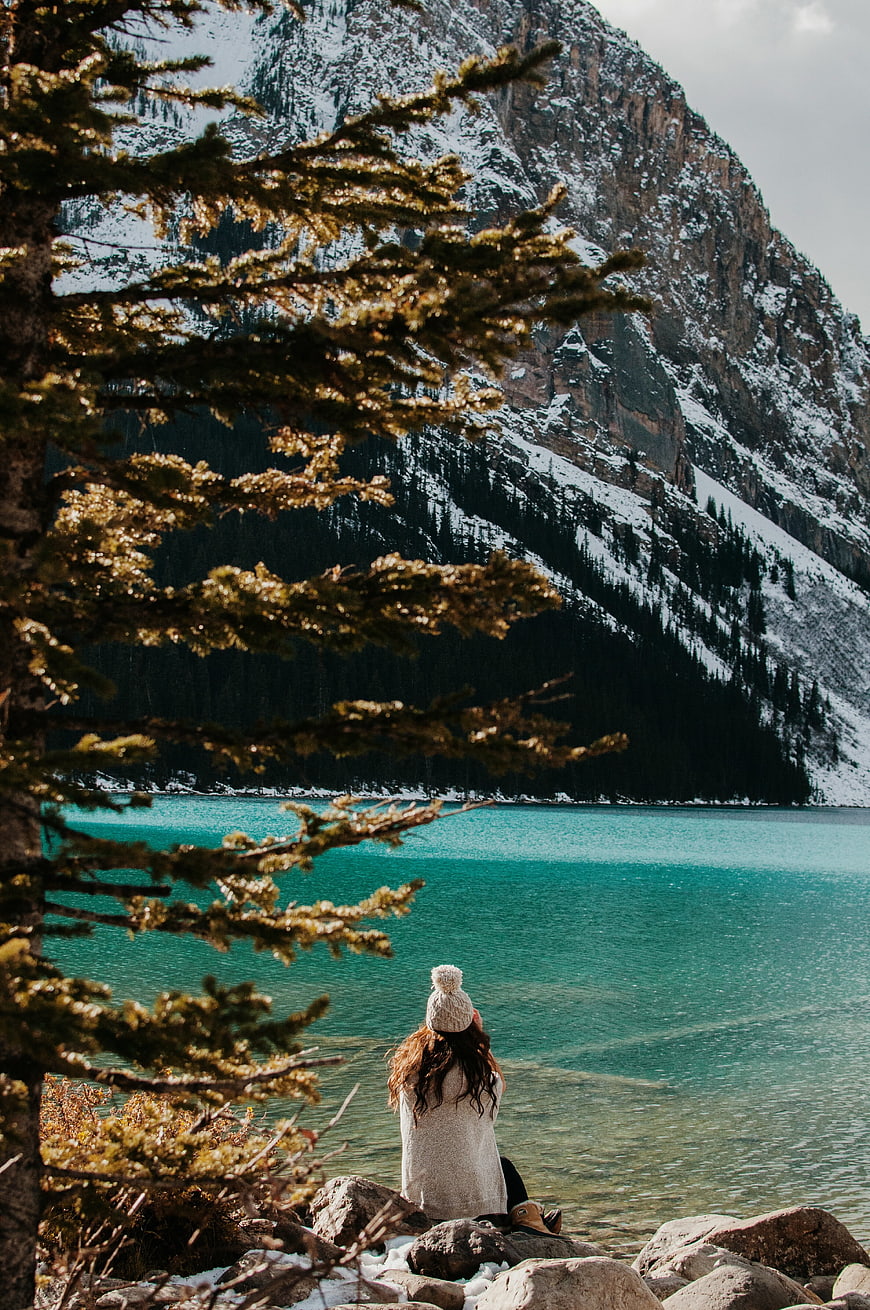 Woman sitting by turquoise alpine lake with snowy mountains