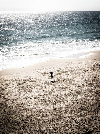 Silhouette of person standing on sandy beach facing sparkling ocean