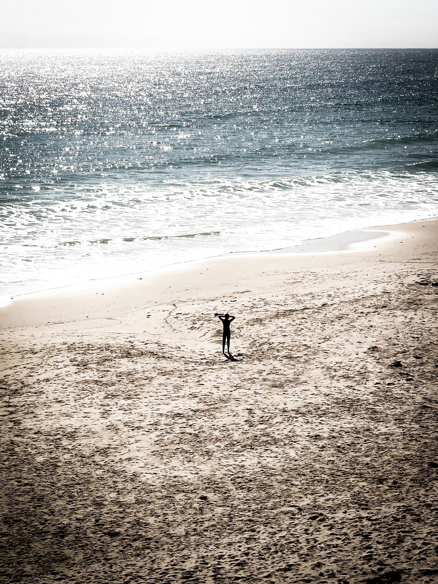 Silhouette of person standing on sandy beach facing sparkling ocean