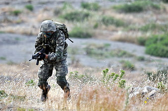 Soldier in camouflage running with rifle through dry field