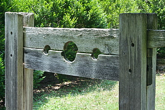 Weathered Wooden Pillory With Circular Holes In Green Garden
