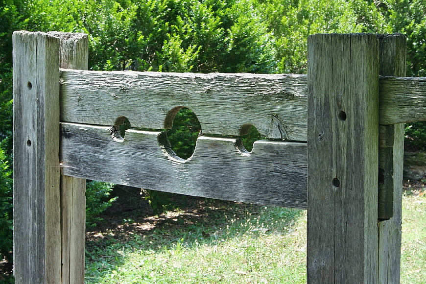 Weathered Wooden Pillory With Circular Holes In Green Garden
