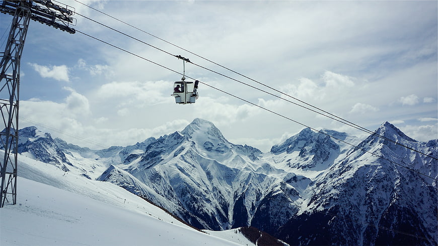 Gondola lift against snowy mountain peaks and blue sky