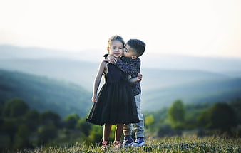 Young brother kissing sister on cheek in scenic outdoor portrait
