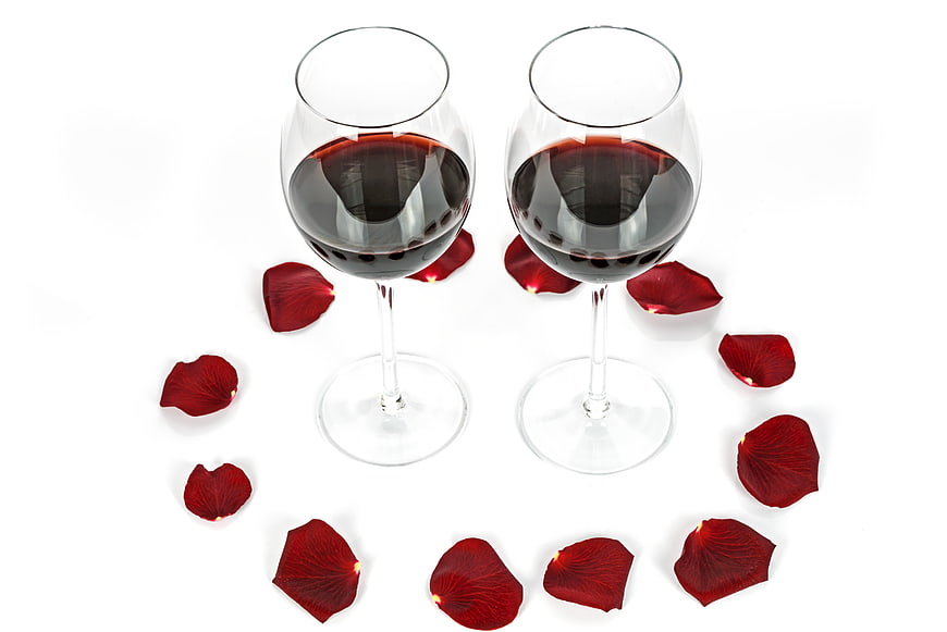 Two glasses of red wine with rose petals on white background