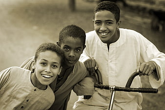 Three smiling boys posing with a bicycle in sepia tone