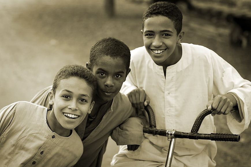 Three smiling boys posing with a bicycle in sepia tone