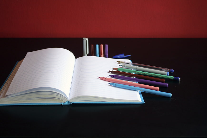 Open Notebook with Colorful Pens on Dark Desk