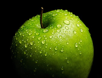 Close-up of a fresh green apple with water droplets on a black background