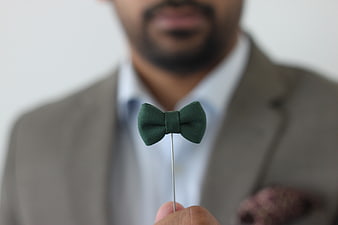 Man holding green bow tie lapel pin in suit