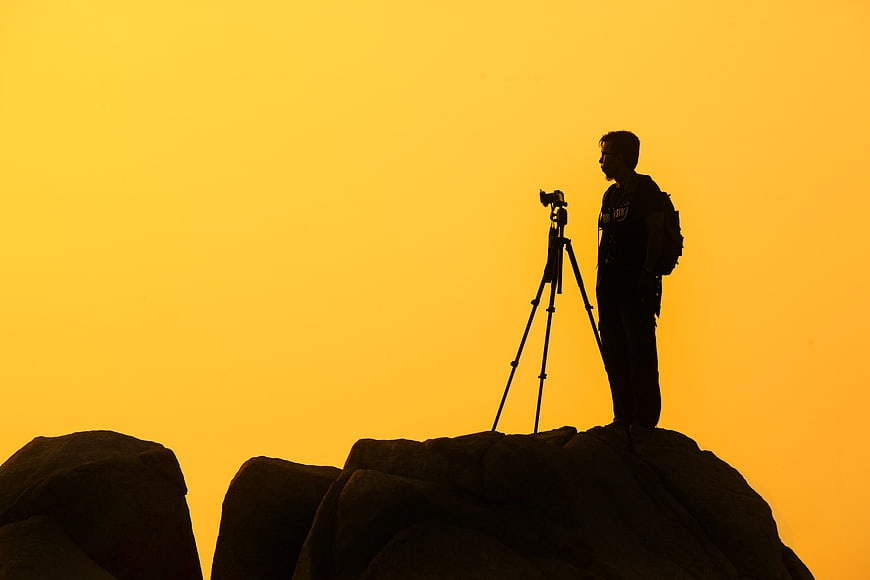 Silhouette of photographer with camera on tripod at sunset