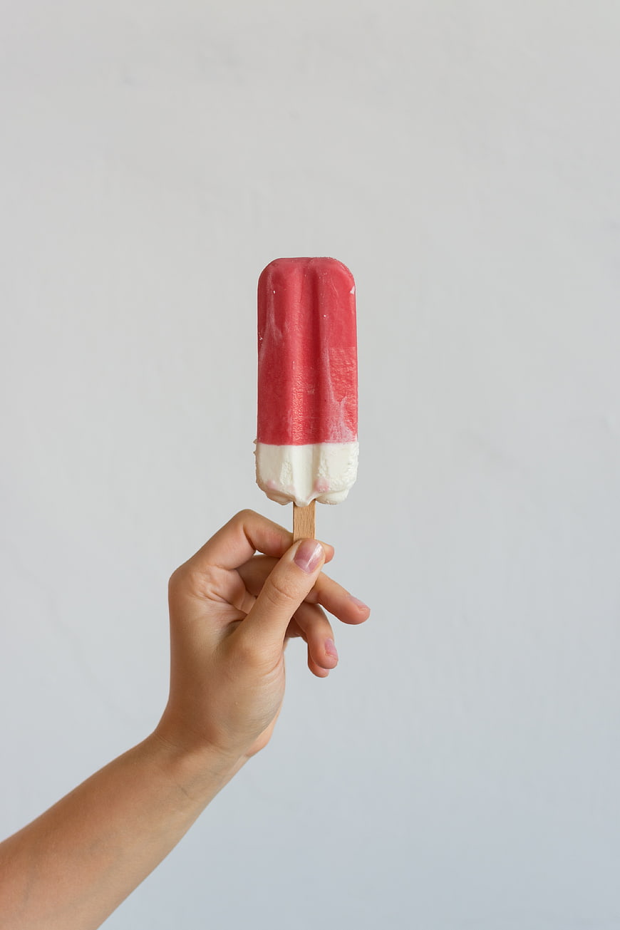 Hand holding red and white popsicle on white background