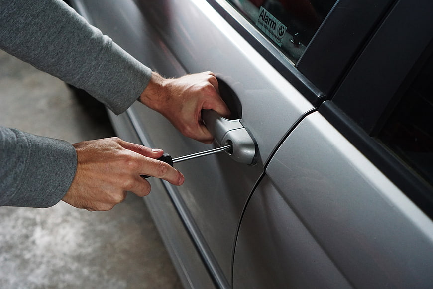 Car thief using screwdriver to break into vehicle door lock
