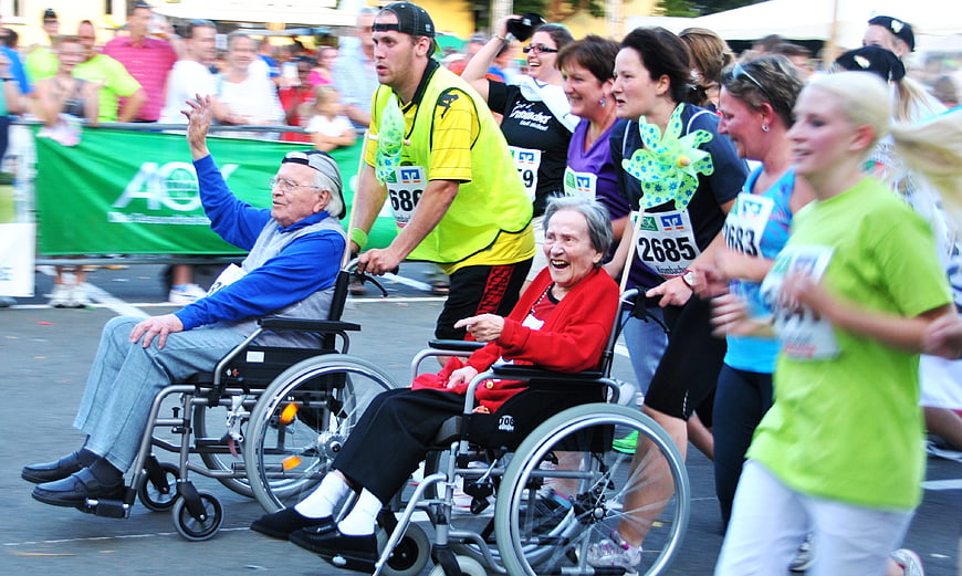 Senior couple in wheelchairs racing with runners at charity event