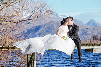 Bride and Groom Kissing on Dock with Mountain Lake Background