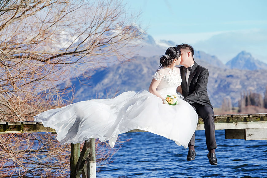 Bride and Groom Kissing on Dock with Mountain Lake Background