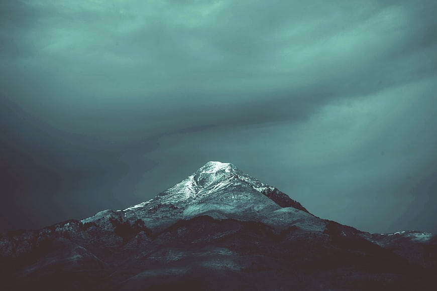Dramatic Snow-Capped Mountain Peak Under Stormy Teal Sky