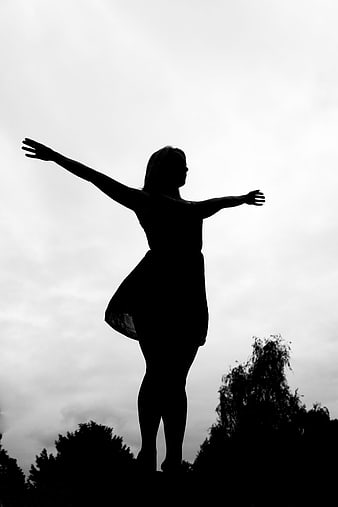 Black and white silhouette of a woman with arms outstretched standing outdoors