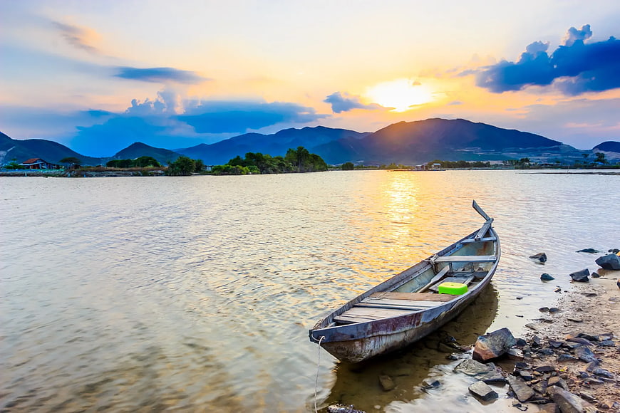 Wooden boat on riverbank at sunset with mountains