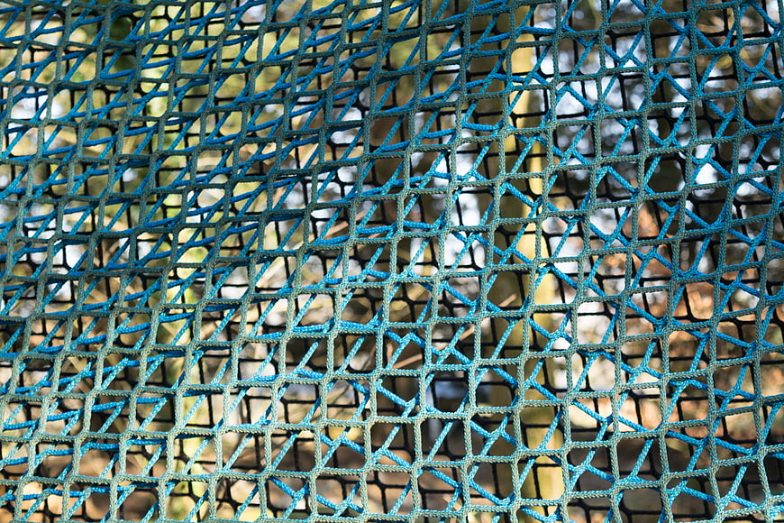 Close-up of blue plastic mesh fence with blurred nature background