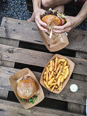 Top view of hands holding burger and fries on wooden table
