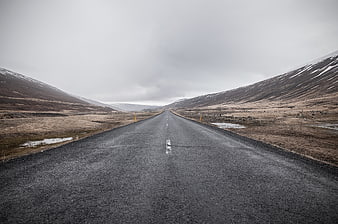 Empty asphalt road stretching through barren mountains under overcast sky