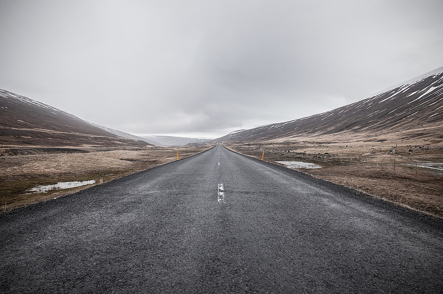 Empty asphalt road stretching through barren mountains under overcast sky