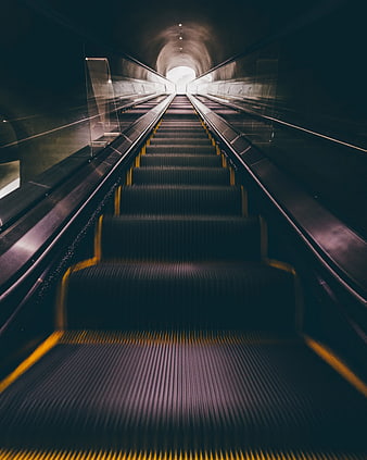 Low angle view of escalator leading to bright tunnel exit