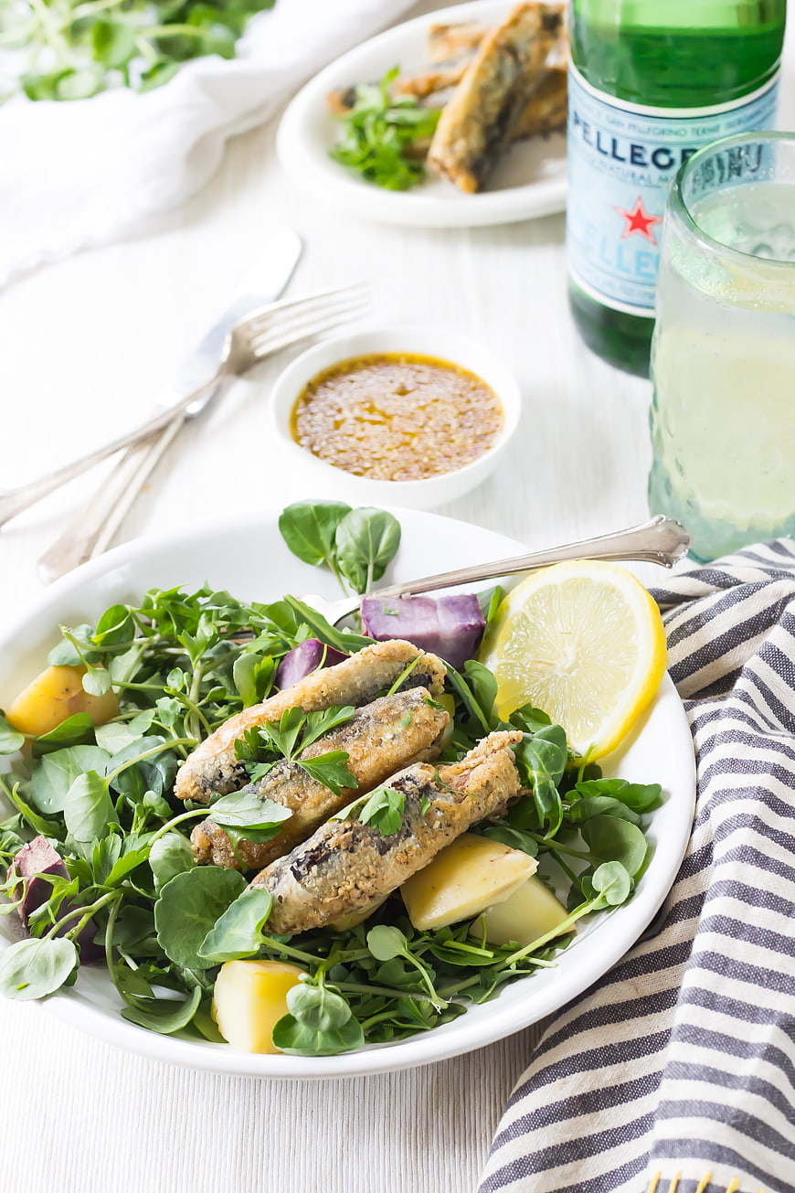 Fried fish salad with lemon and dressing on white table