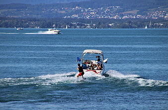 Water skiing behind a motorboat on a sunny lake with distant shoreline